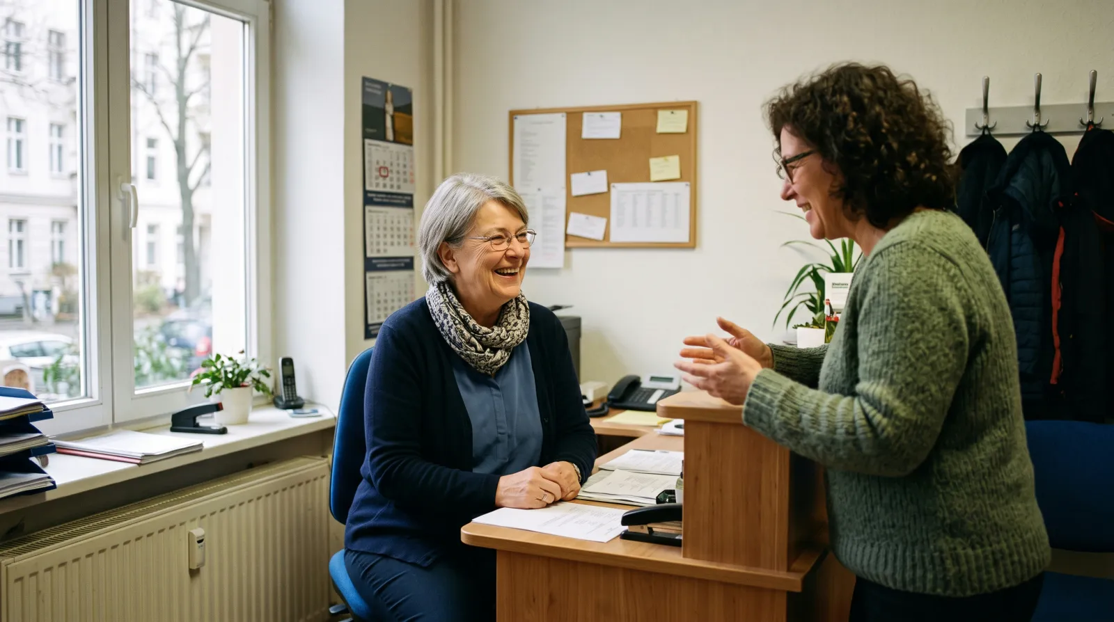 Frau um die 66 im Gespräch mit einer Kollegin in einem kleinen Büro