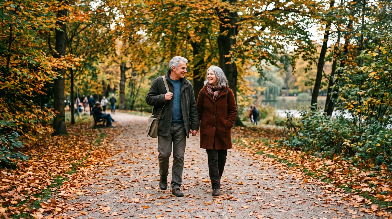 Paar Anfang 60 spaziert im Herbst auf einem baumgesäumten Weg durch einen Park
